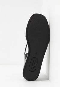 Semelle de sandale noire vue de face avec la taille 38 et une grande lettre « C » embossée près du talon, sur un fond blanc en coin.