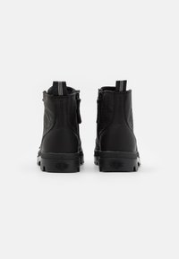 Botas de tobillo de cuero negro con un acabado texturizado, cremallera trasera y costuras en blanco en la lengüeta. Suela de goma con logo.