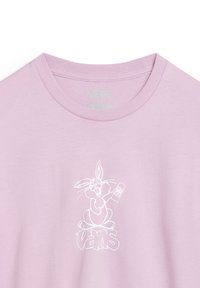 Camiseta rosa claro con cuello redondo, que presenta un gráfico blanco de un conejo de dibujos animados sosteniendo un control remoto y la palabra "VANS" abajo.