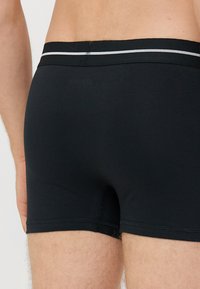 Fekete modal boxer nadrág puha derékkal, fehér csíkkal. Sima textúra és testhezálló kialakítás a kényelem és a tartás érdekében.