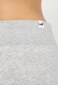 Szary sweter z ribbowanym pasem. Na plecach widoczna jest mała biała metka z logo Puma. Miękka bawełniana tekstura.