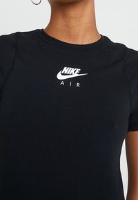 Svart bomullströja med en kroppsnära design, med en vit Nike-logotyp och texten "AIR" på framsidan. Korta ärmar och rund halsringning.