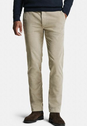 Pantalon en velours côtelé beige avec une coupe droite, présentant un léger côtelage vertical et des poches latérales. Complété par des bottines chelsea marron foncé.