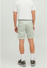 Světle zelené bavlněné šortky s ohrnutými lemy, obsahující dvě zadní kapsy. Nosené s bílým tričkem a šedými sportovními botami.