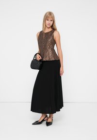Koperpatronen mouwloze top gecombineerd met een zwarte geplooide maxirok, geaccessorieerd met een kleine zwarte handtas en platte schoenen.