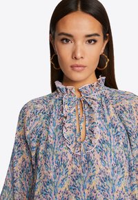 Floral blouse in soft fabric with a ruffled neckline, keyhole detail, and vibrant purple, blue, and yellow colors with pleated texture.