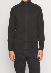 Ciemnoszary sweter na zamek z wysokim kołnierzem, ściągaczami na rękawach i u dołu, z subtelnymi akcentami na ramionach oraz małym logo na piersi.