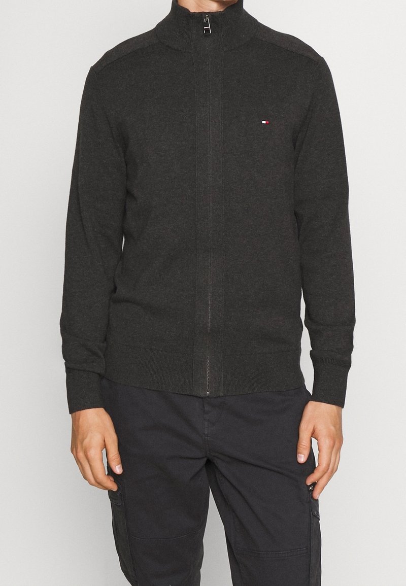 Ciemnoszary sweter na zamek z wysokim kołnierzem, ściągaczami na rękawach i u dołu, z subtelnymi akcentami na ramionach oraz małym logo na piersi.