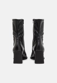 Czarne skórzane botki za kostkę o gładkiej fakturze, z zamkami błyskawicznymi i kwadratowymi obcasami; posiadają przeszycia i dopasowany fason.