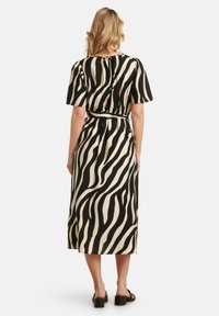 Zwarte en crèmekleurige midi-jurk met zebra-print, korte mouwen, een ceintuur rond de taille en een keyhole-detail aan de achterkant. Gladde stof met een vloeiende silhouette.