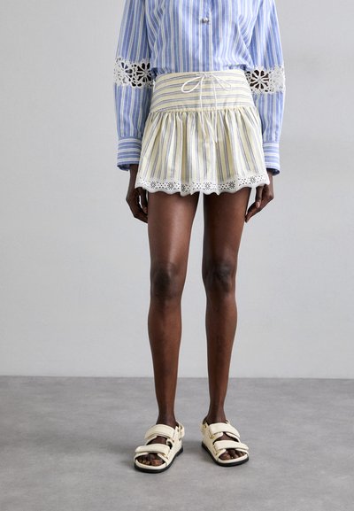 Jupe rayée jaune et blanche avec un ourlet volanté et une bordure en dentelle festonnée, associée à une chemise rayée bleue avec des accents en dentelle.