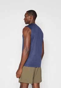 Haut de sport sans manches bleu marine avec un col rond, texture lisse et coutures minimales. Associé à un short vert olive.