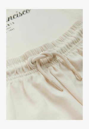 Világos bézs szabadidőnadrág, elasztikus derékpánttal, zsinórral, műanyag végződéssel és puha, texturált anyagból készült.