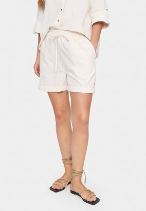 Shorts clairs et texturés avec une taille élastique et un cordon de serrage, dotés d'ourlets roulés. Associés à des sandales plates à lanières.