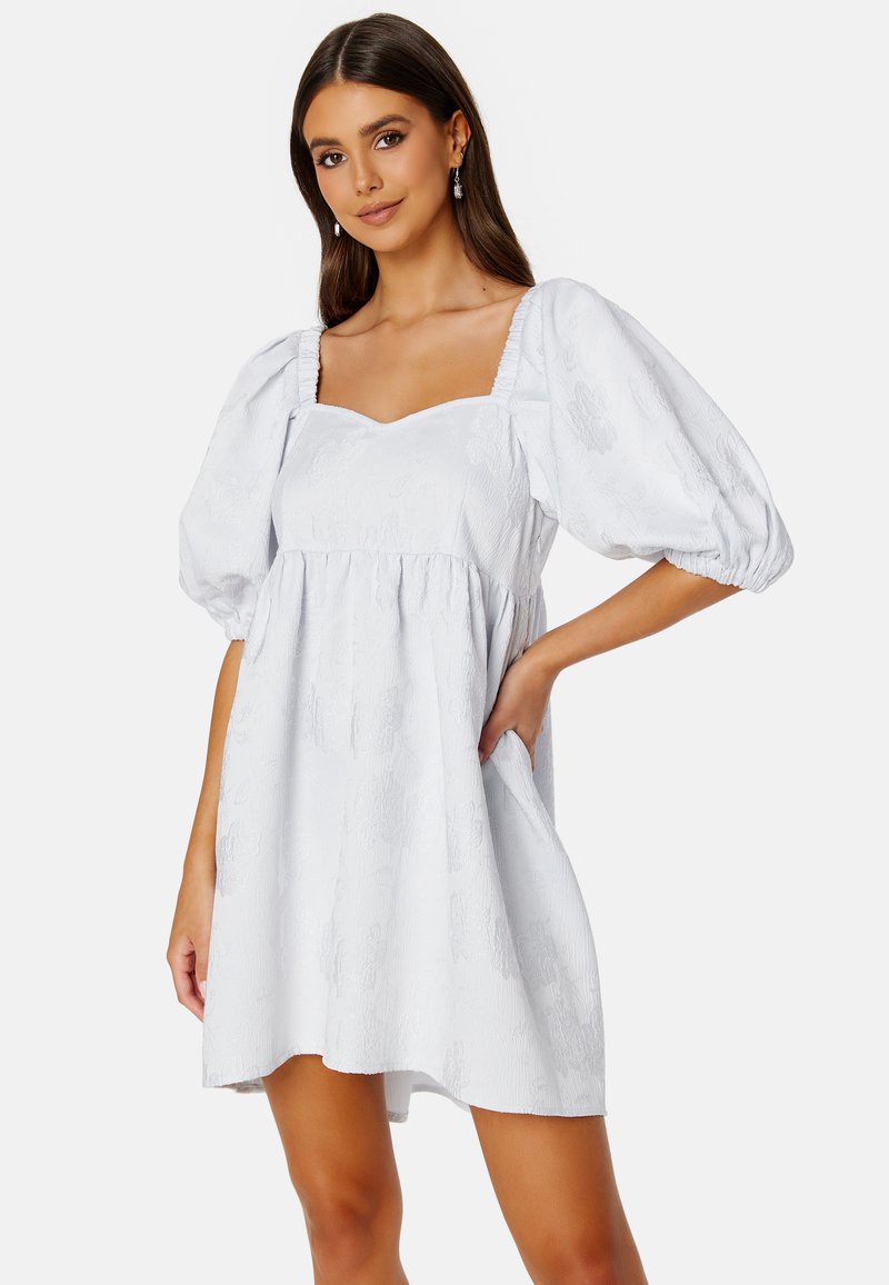 Bílé šaty s balónovými rukávy a čtvercovým výstřihem, zdobené texturovaným květinovým vzorem, s uvolněným střihem a bočními kapsami.