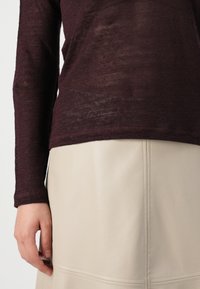 Haut bordeaux à manches longues en maille légère et texturée, associé à une jupe en simili cuir beige avec des détails de coutures.