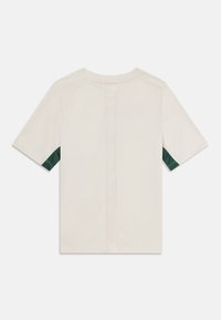 Off-white kratki rokav s temno zelenimi mrežastimi detajli pod rokavi in navpično mrežasto črto na sredini hrbta.