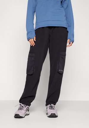 Zwarte cargobroek met twee zijzakken, elastische boorden en een gladde textuur, gecombineerd met een blauwe sweatshirt en lichtpaarse schoenen.