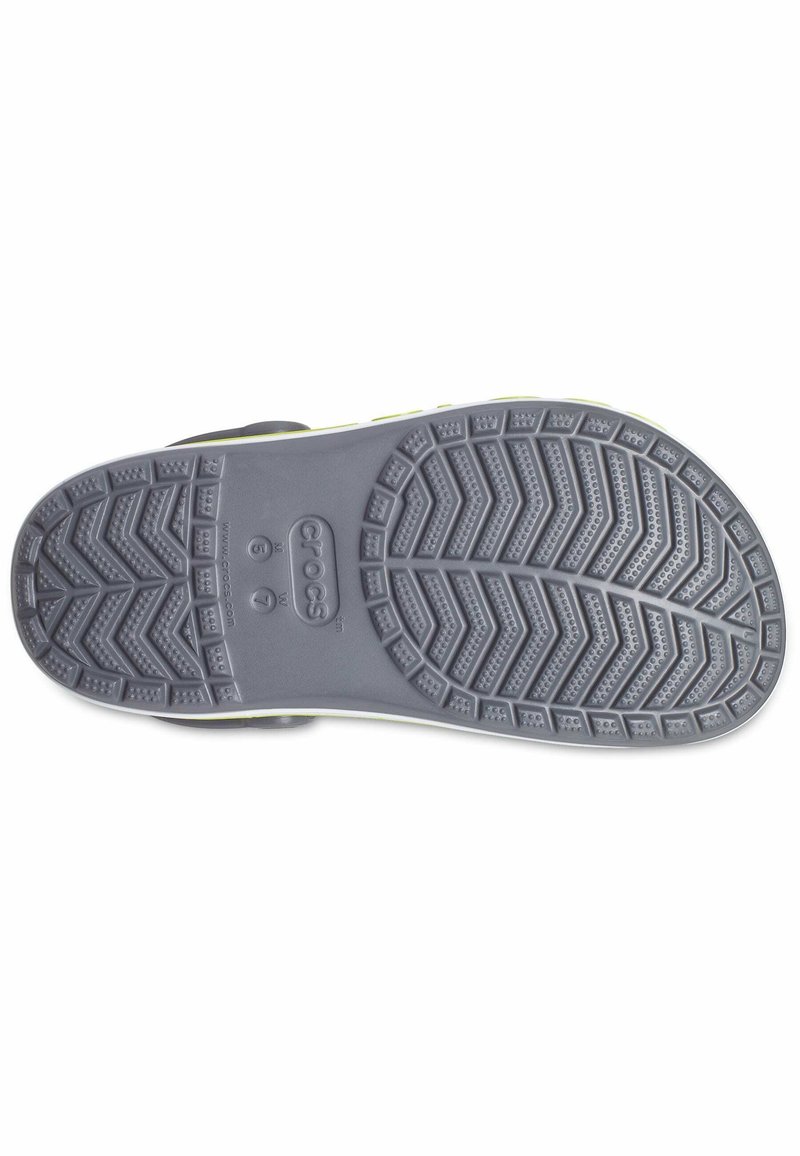 Grijze rubberen zool met een zigzag- patroon en kleine ronde noppen. Bevat merknaam en een gladde rand met een gele accent.