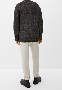 Maglione nero lavorato a maglia con una finitura testurizzata, abbinato a pantaloni beige chiaro e stivali neri. Il maglione presenta una vestibilità ampia e maniche lunghe.
