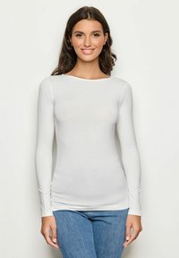 Langarm-weißer Oberteil aus glattem Stoff, mit rundem Halsausschnitt und figurbetontem Design, kombiniert mit blauen Jeans. Keine Muster oder Akzente.