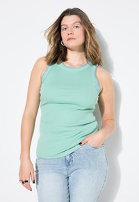 Top a maniche corte righe verde chiaro con bordi testurizzati blu lungo il collo e le aperture delle maniche, abbinato a jeans aderenti blu chiaro.