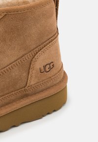 Stivale alla caviglia in suede marrone chiaro con una finitura testurizzata, dotato di suola in gomma e del logo UGG impresso sul lato.