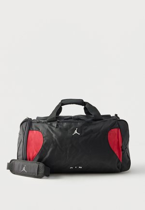 Bolsa de deporte tipo duffel negra y roja con asas superiores, correa de hombro ajustable, bolsillo delantero con cremallera y logo blanco de Jumpman en el frontal y la correa.