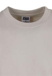 T-shirt beige en coton à col rond avec une texture unie et une étiquette de taille de la marque Urban Classics, montrant une discrète étiquette de marque à l'intérieur du col.