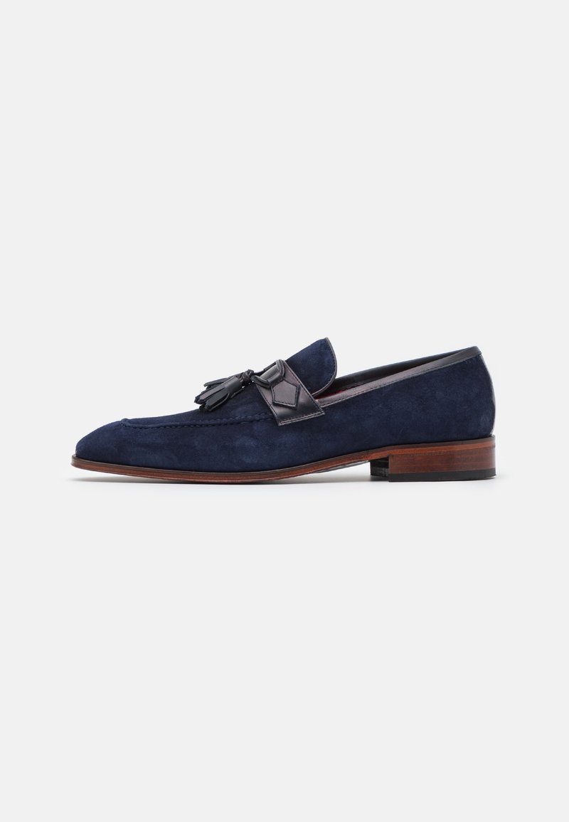Mocassin homme en daim bleu marine avec pampilles en cuir noir et petit talon en bois marron, vu de côté sur fond blanc.