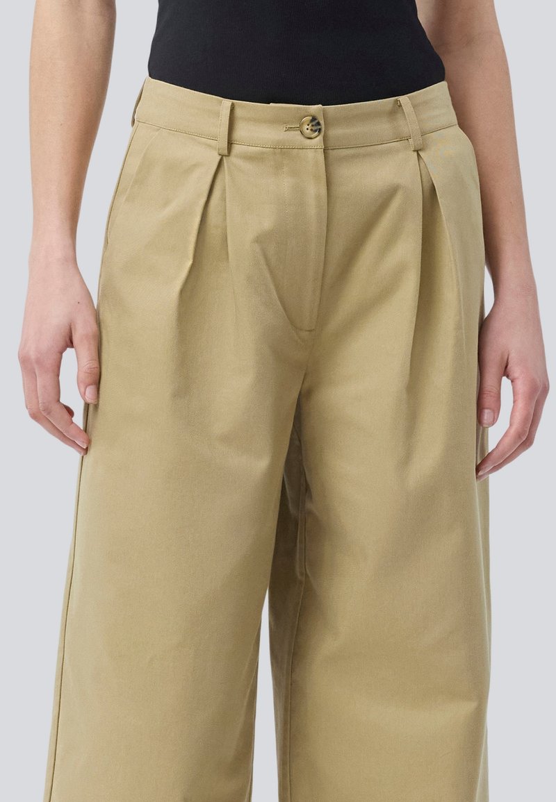 Beige hochgeschnittene Hose mit Falten, mit einem Knopfverschluss und seitlichen Taschen. Aus einem leichten Stoff mit glatter Textur gefertigt.