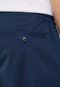 Pantaloni corti blu navy con vita elasticizzata e una tasca sul retro con un bottone nero e dettagli di cucitura. Tessuto liscio e leggero.