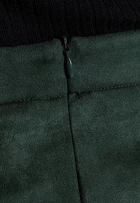 Tmavě zelené semišové kalhoty s hladkým povrchem a zipovým uzávěrem v pase, s pečlivým prošíváním podél švů.