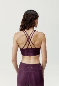 Sujetador deportivo burdeos con tirantes entrecruzados, hecho de un material suave y elástico; combinado con leggings de alta cintura a juego que presentan acentos mínimos.