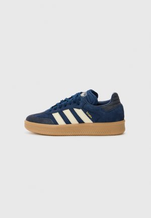 Baskets Adidas Samba bleu marine avec des rayures crème, semelle en gomme et texte doré "SAMBA" sur le côté, présentées de l’extérieur.