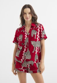 Roter Schlafanzug bestehend aus einem kurzärmligen, kragenlosen Shirt und Shorts, geschmückt mit schwarz-weißen Leopardenmustern und pinken Wellenmustern.