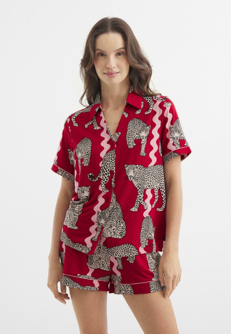 Roter Schlafanzug bestehend aus einem kurzärmligen, kragenlosen Shirt und Shorts, geschmückt mit schwarz-weißen Leopardenmustern und pinken Wellenmustern.