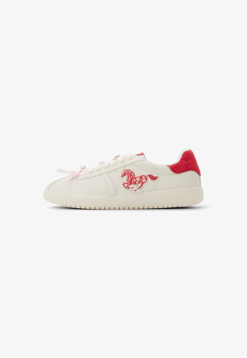 Sneaker bianca con patch rosso sul tallone, ricamo rosso di cavallo e fiore, lacci decorati con perle e suola in gomma su sfondo bianco.