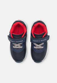 Scarpe sportive blu navy con tomaia in rete, foderate in rosso e con cinturino in velcro; presentano lacci grigi e una suola in gomma testurizzata.