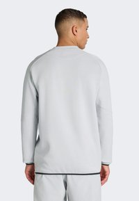 Jasnoszara bluza z długim rękawem, z prążkowanym dekoltem i sportowym krojem, z subtelnym detalem na ramieniu.