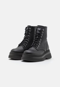 Botas de tobillo de cuero negro con una gran plataforma, diseño con cordones, ojetes de metal y una cremallera lateral. Parte superior texturizada con suela de goma.