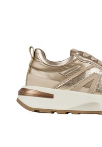Gouden en beige sneaker met dikke witte zool, gestructureerd zijpaneel, trekhaak op de hiel en metalen accenten.