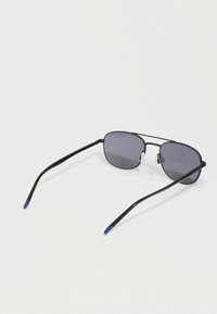 Μαύρα ηλιοφάνεια με μεταλλικό σκελετό και σκούρους ορθογώνιους φακούς, με μπλε άκρα στους βραχίονες, ακουμπισμένα σε μια ανοιχτόχρωμη επιφάνεια.