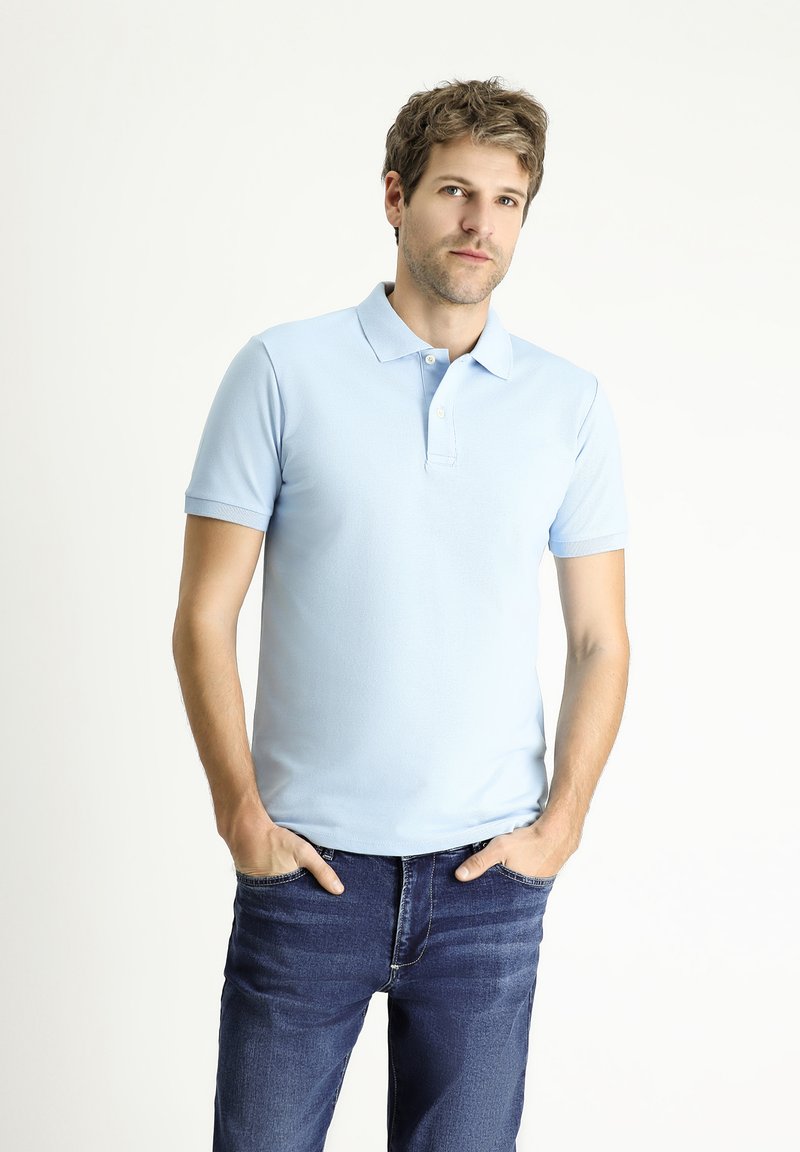 camisa polo azul claro con cuello clásico, mangas cortas y textura lisa, combinada con jeans de mezclilla azul oscuro.