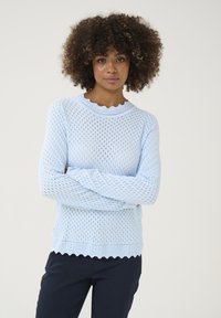 Hellblau gestrickter Pullover mit einem Netzdesign, gewelltem Ausschnitt und strukturierten Ärmeln, kombiniert mit marineblauen Hosen.