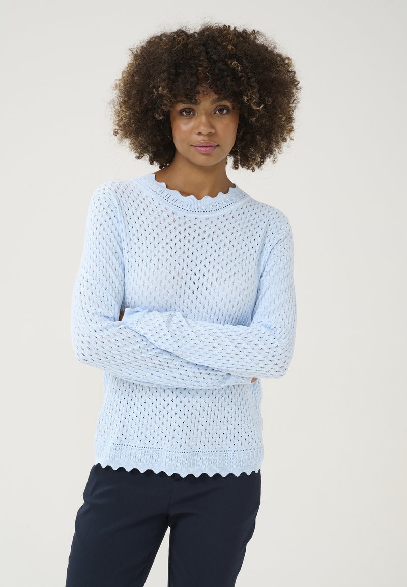 Hellblau gestrickter Pullover mit einem Netzdesign, gewelltem Ausschnitt und strukturierten Ärmeln, kombiniert mit marineblauen Hosen.