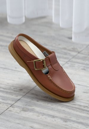 Chaussure en cuir marron à enfiler avec boucle, coutures détaillées et semelle en caoutchouc beige clair sur un fond de sol en marbre.