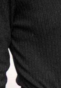 Schwarzer gerippter Strickstoff mit einer strukturierten Oberfläche, die subtile Variationen und kleine Flusen zeigt und eine enganliegende Form bildet.