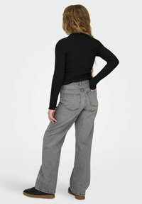 Juodas ribuotas ilgomis rankovėmis megztinis derinamas su pilkomis, aukštos juosmens ir laisvo kirpimo džinsais. Džinsuose yra du galiniai kišenės ir subtilūs siuvimo akcentai.