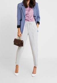 Light gray, tailored joggers with white side stripes, paired with a lavender blouse and a blue blazer, complemented by a brown handbag and white heels.